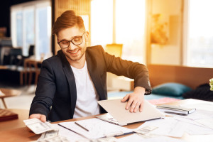 Freelancer man counting money closing laptop sitting at desk.